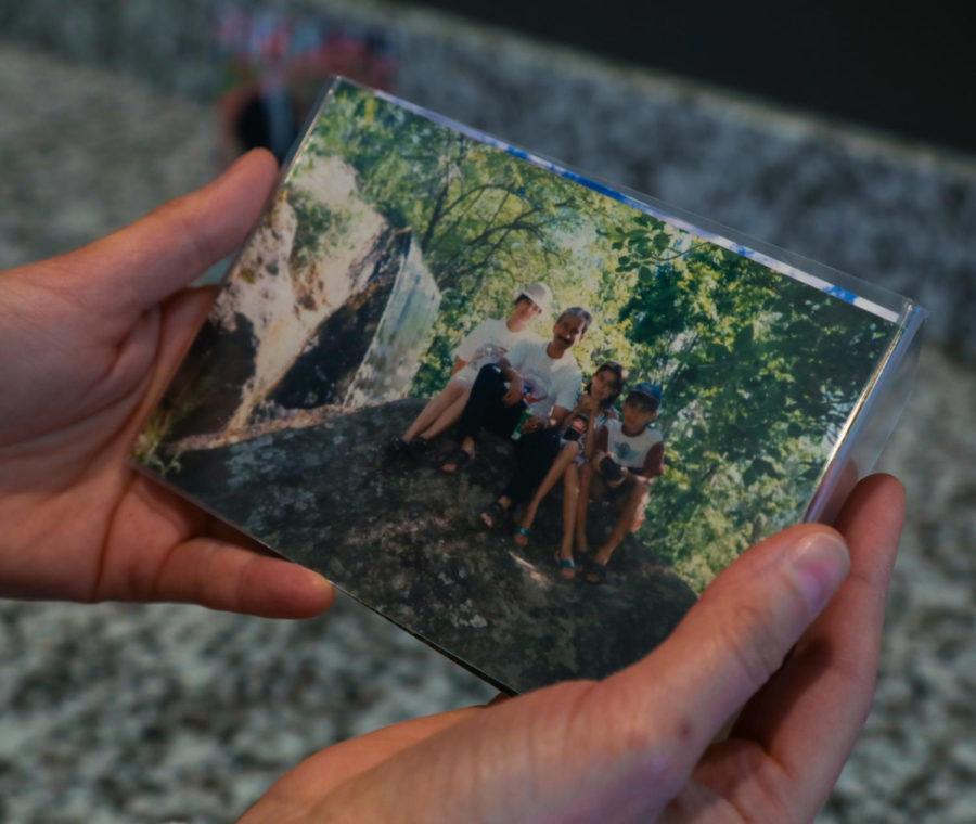 Pakiza holds a photo of her family, four people sitting on a rock in the forest as sun peeks through the trees.